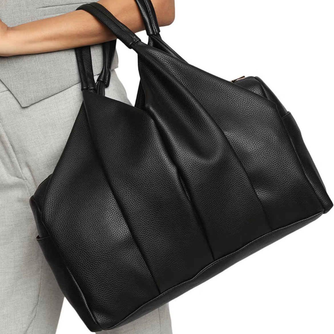 Black leather handbag held by a person wearing gray pants on a white background