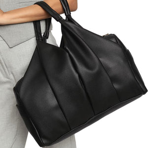 Black leather handbag held by a person wearing gray pants on a white background